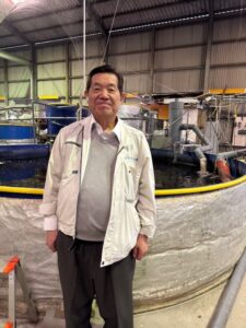 ジャパンマリンポニックス藤田工場の水槽前に立つ内尾社長