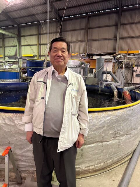 ジャパンマリンポニックス藤田工場の水槽前に立つ内尾社長